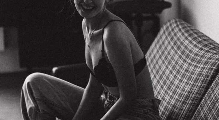 Smiling Young Woman in Bra and Jeans Sitting on the Couch